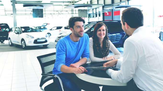 man and woman negotiating with car dealer in the showroom