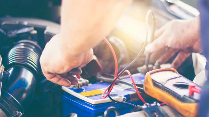 Mechanic inspects battery with handheld multimeter (voltmeter)